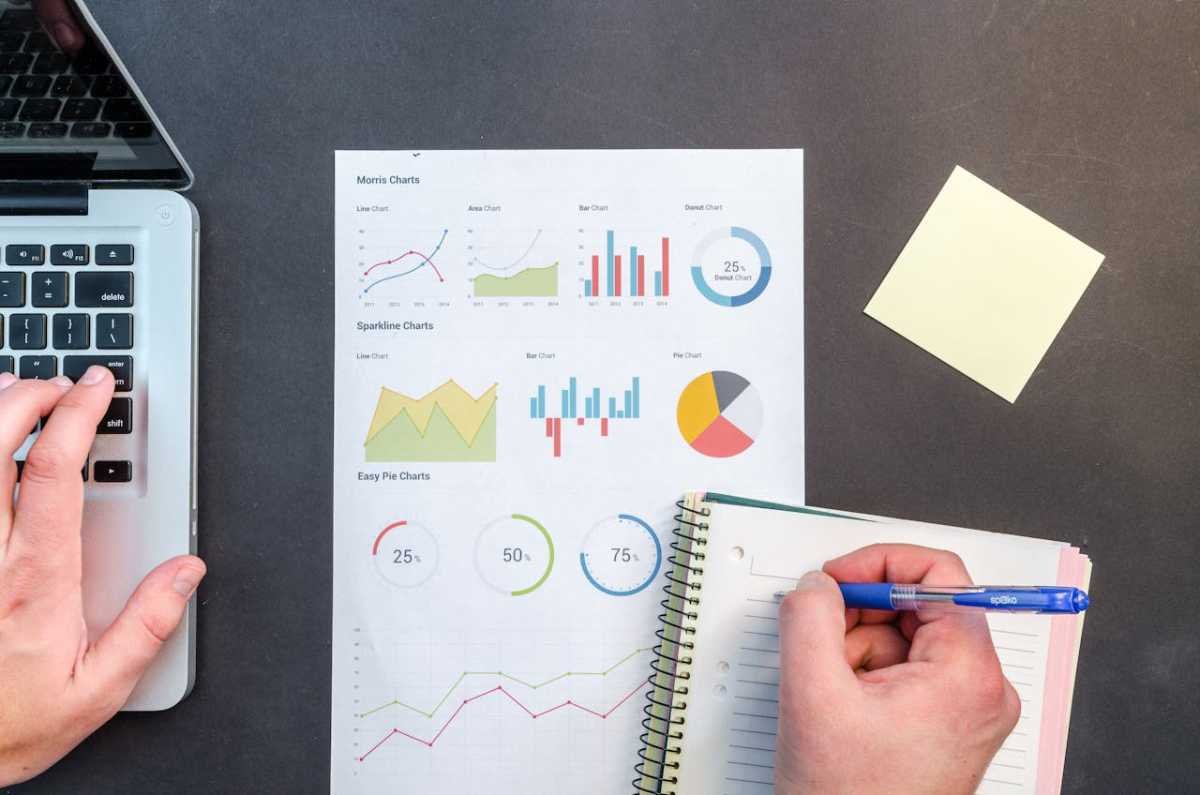 Man writing notes in a notebook with a document showing graphs, representing SEO analysis and evaluation of guest post quality